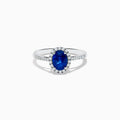 The 14K White Gold Oval Blue Sapphire and Diamond Ring features an oval blue sapphire center, a halo of sparkling diamonds, and additional diamonds set along the band.