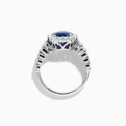 The 18K White Gold GIA Certified Cushion Cut Blue Sapphire and Diamond Ring features a striking cushion cut blue sapphire center, round diamond halo, and baguette-cut diamonds on the band, shown against a white background.