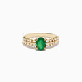 The 14K Yellow Gold Emerald and Diamond Ring showcases an oval green emerald center, framed by two rows of round diamonds on each side, set in yellow gold against a white background.