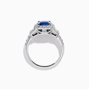 The Royale Bleu Platinum Blue Sapphire Halo Ring showcases a large cushion-cut sapphire surrounded by sparkling diamonds on a platinum band, set against a white background for a timeless, elegant look.