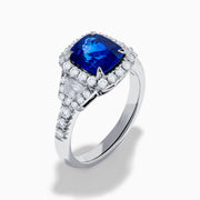 The Royale Bleu Platinum Blue Sapphire Halo Ring showcases a large cushion-cut sapphire surrounded by sparkling diamonds on a platinum band, set against a white background for a timeless, elegant look.