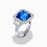 The Royale Bleu 18K White Gold Blue Sapphire and Diamond Halo Ring showcases a cushion-cut blue sapphire center with a double diamond halo and diamond side accents, elegantly set against a white background.