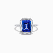 The Nahla Siri 14K White Gold Tanzanite and Diamond Ring features a large emerald-cut blue tanzanite, haloed by small white diamonds with additional diamonds set along the band.