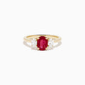 The 14K Yellow Gold Ruby and Diamond Three-Stone Ring showcases a striking oval ruby center with two oval white diamonds, set in yellow gold and displayed on a white background.