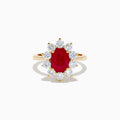 The 14K Yellow Gold Natural Ruby and Diamond Lady Di Ring showcases an oval natural ruby center with a halo of round white diamonds, set against a white background.