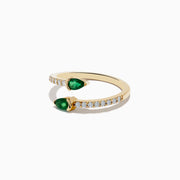 The 14K Yellow Gold Emerald and Diamond Bypass Ring showcases two pear-shaped emeralds on an open gold band accented by round white diamonds, elegantly displayed on a white background.