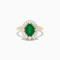 The 14K Yellow Gold Emerald and Diamond Ring showcases an oval emerald center accented by a halo of round white diamonds, displayed against a white background.