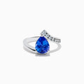 The Nahla Siri 14K White Gold Floating Tanzanite and Diamond Ring features a large pear-shaped blue tanzanite center and a curved band with sparkling round white diamonds on one side, set against a plain white background.