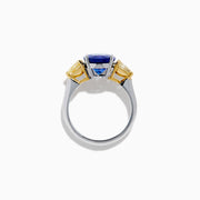 A striking 18K two tone gold ring featuring a large oval blue tanzanite center and two pear-shaped yellow diamonds on each side, displayed against a plain white background.