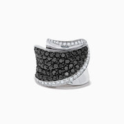 The 14K White Gold Black and White Diamond Ring features a wide, curved design with black and white diamonds at the center, bordered by clear stones along the edges, all set against a white background.