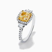 The Canare 18K Two Tone Gold White and Yellow Diamond Ring features a cushion-cut yellow diamond center, framed by a halo of white diamonds and more diamonds set along the band in elegant white gold.