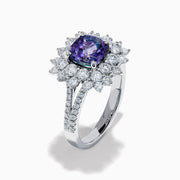 The 18K White Gold GIA Certified Zoisite and Diamond Ring features a cushion-cut blue-purple zoisite center stone with a starburst diamond halo, creating a striking look against the white gold setting.