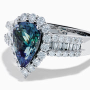 The 18K White Gold GIA Certified Pear Zoisite and Diamond Ring showcases a striking blue-green gemstone accented by round diamonds, with more diamonds along the band for extra brilliance and certified authenticity.