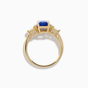 The Nahla 14K Yellow Gold Tanzanite and Diamond Ring showcases a rectangular blue tanzanite center, with two round diamonds and two baguette-cut white stones on each side, displayed on a white background.