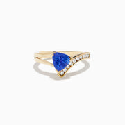 The Nahla 14K Yellow Gold Tanzanite and Diamond Ring features a triangular blue tanzanite center, accented by a curved row of sparkling round white diamonds on one side of the band.