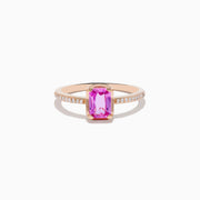 The 14K Rose Gold Pink Sapphire and Diamond Solitaire Ring features a rectangular pink sapphire centerpiece and small round diamonds on the band, shown against a white background.