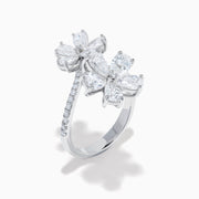 The Lab Grown Pear and Round Diamond 2.75ct Flower Bypass Ring in 14K White Gold features two flower designs with pear-shaped and round diamonds on a partially encrusted band, set against a white background for an elegant look.