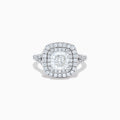 The Lab Grown Cushion Diamond Double Halo Ring in 14K White Gold features a cushion-cut center diamond, double halo of smaller diamonds, and additional diamonds along the band.