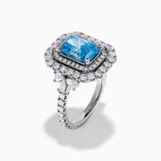 The Lab Grown Blue Diamond Double Halo Cocktail Ring in 14K White Gold features a rectangular blue center, round white diamonds on the band, and is displayed against a white background.