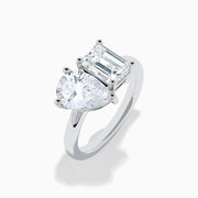The Lab Grown Diamond Toi Et Moi Ring in 14K White Gold showcases emerald-cut and pear-shaped lab diamonds set side by side on a sleek band, displayed against a white background.