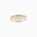 The Lab Grown Round Diamond Bezel Ring in 14K Yellow Gold features a simple band with a single bezel-set round white diamond at the center, shown on a white background.