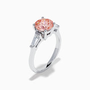 The Lab Grown Pink and White Diamond 3 Stone Ring in 14K White Gold features a striking round pink center stone with two rectangular white diamonds on each side, set against a white background.