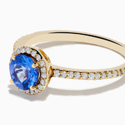 The Nahla 14K Yellow Gold Tanzanite and Diamond Ring showcases a round tanzanite center, encircled by a halo of clear diamonds and accented with additional diamonds along the band.