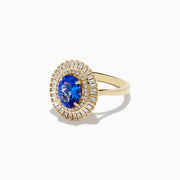 The Nahla Siri 14K Yellow Gold Tanzanite and Diamond Ring features an oval-cut tanzanite center with two halos of baguette and round diamonds, beautifully presented on a plain white background.