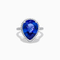 The 14K White Gold Pear Shape Tanzanite and Diamond Halo Ring features a pear-shaped blue tanzanite surrounded by a diamond halo on a delicate white gold band, displayed against a white background.