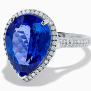 The 14K White Gold Pear Shape Tanzanite and Diamond Halo Ring features a pear-shaped blue tanzanite surrounded by a diamond halo on a delicate white gold band, displayed against a white background.