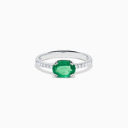 The 14K White Gold East West Oval Emerald and Diamond Ring showcases a striking green oval emerald set horizontally, accented by sparkling diamonds along the band.