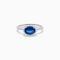 The 14K White Gold East West Oval Blue Sapphire and Diamond Halo Ring showcases an oval blue sapphire encircled by a diamond halo, with extra diamonds accenting the band for added brilliance.