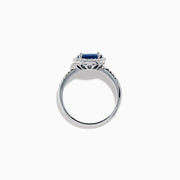 The 14K White Gold East West Oval Blue Sapphire and Diamond Halo Ring showcases an oval blue sapphire encircled by a diamond halo, with extra diamonds accenting the band for added brilliance.
