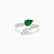 The 14K Two Tone Gold Emerald and Diamond Toi et Moi Ring features a pear-shaped green emerald and a pear-shaped white diamond, accented by sparkling small diamonds on the band.