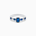 The Royal Bleu 14K White Gold Blue Sapphire and Diamond Ring features a rectangular blue sapphire center, flanked by square blue stones and diamonds on a sleek band against a plain white background.