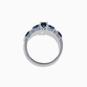 The Royal Bleu 14K White Gold Blue Sapphire and Diamond Ring features a rectangular blue sapphire center, flanked by square blue stones and diamonds on a sleek band against a plain white background.