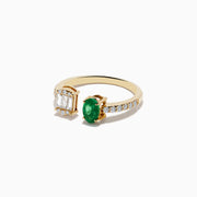 The 14K Yellow Gold Emerald and Diamond Toi Et Moi Ring features a row of diamonds on the band, an emerald-cut diamond cluster on one side, and a striking green oval emerald gemstone on the other.