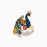 The Safari 14K Yellow Gold Multi Sapphire Peacock Ring features vibrant blue, green, yellow, pink, and orange sapphires with detailed feathers and a jeweled crown, set against a white background.
