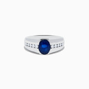 The Mens 14K White Gold Sapphire and Diamond Ring features a large oval blue sapphire at the center, accented on each side by rows of small round white diamonds set into the stylish band.