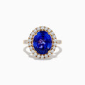 The Nahla Siri 14K Yellow Gold Tanzanite and Diamond Ring features a large oval blue tanzanite center stone encircled by a halo of small round white diamonds, displayed on a plain white background.