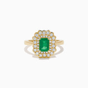 The Brasilica 14K Yellow Gold Emerald and Diamond Double Halo Ring showcases a rectangular green emerald at the center, accented by two rows of sparkling round white diamonds in an elegant scalloped halo design.