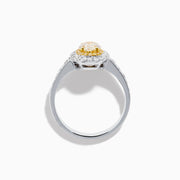 The Canare 18K Two Tone Gold White and Yellow Oval Diamond Ring features a large yellow diamond at the center, a halo of small round white diamonds, and additional diamonds set along the elegant band.
