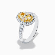 The Canare 18K Two Tone Gold White and Yellow Oval Diamond Ring features a large yellow diamond at the center, a halo of small round white diamonds, and additional diamonds set along the elegant band.