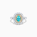 The 18K Two Tone Gold Paraiba and Diamond Double Halo Ring features an oval Paraiba centerpiece, surrounded by radiant yellow and white diamonds in a double halo, creating a striking layered effect.