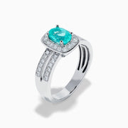 The 18K White Gold Paraiba and Diamond Halo Ring features an oval Paraiba center gemstone, encircled by sparkling diamonds and set on an elegant split shank band adorned with additional diamonds.