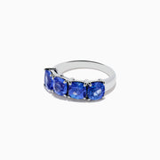 The Nahla Siri 925 Silver Tanzanite Ring showcases four large, cushion-cut blue gemstones set in a row, elegantly displayed on a plain white background.