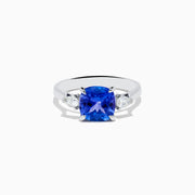 The Nahla Siri 14K White Gold Tanzanite and Diamond Ring features a large cushion-cut blue tanzanite center stone, accented by two smaller white diamonds on each side, set against a white background.