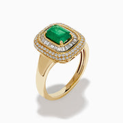 The 14K Yellow Gold Emerald and Diamond Double Halo Ring features an emerald-cut green gemstone at the center, framed by two rows of round and baguette diamonds in a rectangular halo setting.