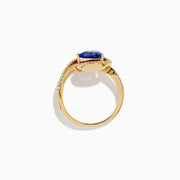 The 14K Yellow Gold Trillion Tanzanite and Diamond Swirl Ring showcases a triangular blue tanzanite center framed by a swirl of white diamonds, all set against a plain white background.