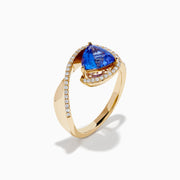 The 14K Yellow Gold Trillion Tanzanite and Diamond Swirl Ring showcases a triangular blue tanzanite center framed by a swirl of white diamonds, all set against a plain white background.